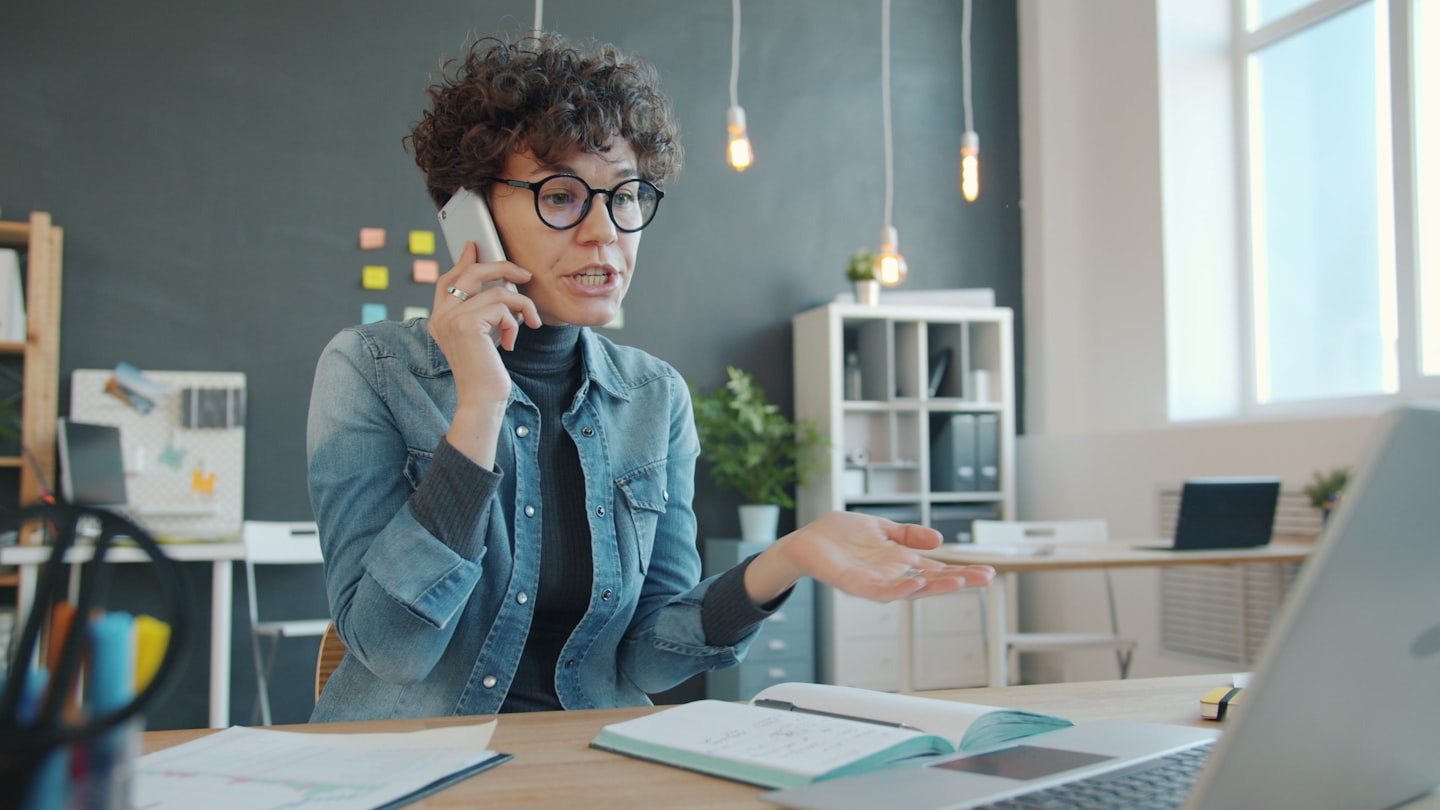 Woman talking on phone at desk with laptop Woman talking on phone at desk with laptop